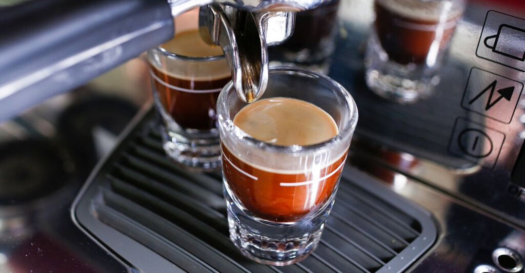 Close up of espresso maching and two espresso shot glasses with dark coffee and creamy top.